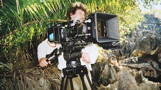 Kameramann an einer 35-mm-Filmkamera zwischen Kalksteinfelsen und Palmen