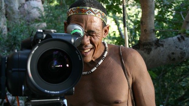 Lächelnder Mann mit Stirnband blickt durch den Sucher einer großen Filmkamera