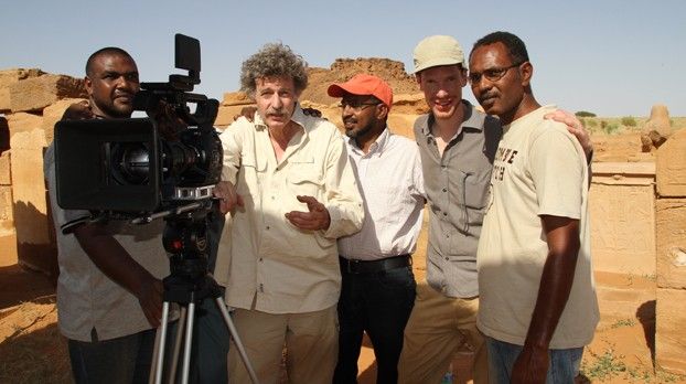 Fünf Männer mit Filmkamera auf Stativ vor antiken Ruinen aus Sandstein