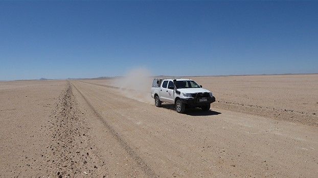 Geländewagen auf einer Sandpiste in weiter Wüstenebene
