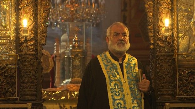 Geistlicher mit weißem Bart und goldbesticktem Gewand in einer prunkvoll geschmückten Kirche