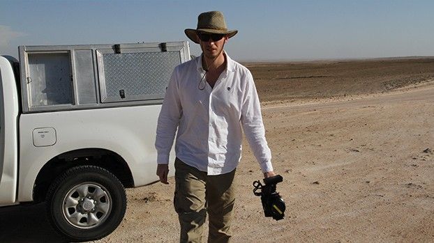 Mann mit Hut und Kamera neben einem Geländewagen in der Wüste