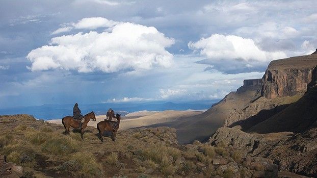 Zwei Reiter auf einem Hochplateau vor Felsabbrüchen und Wolkenhimmel