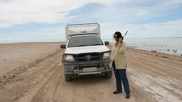 Frau mit Satellitentelefon neben einem Geländewagen in der Etoscha-Pfanne