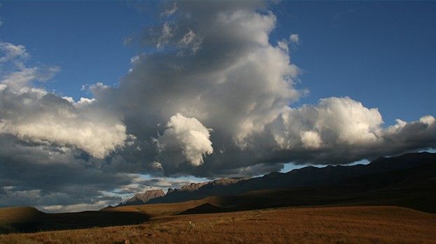 Hohe Wolkentürme über einer weiten Ebene mit Bergkette