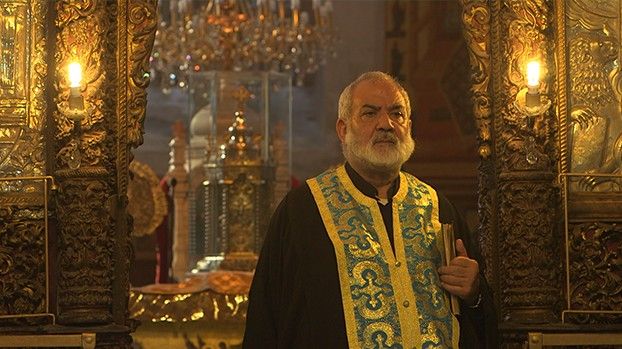 Griechisch-orthodoxer Priester in goldbesticktem Gewand vor vergoldeter Ikonenwand